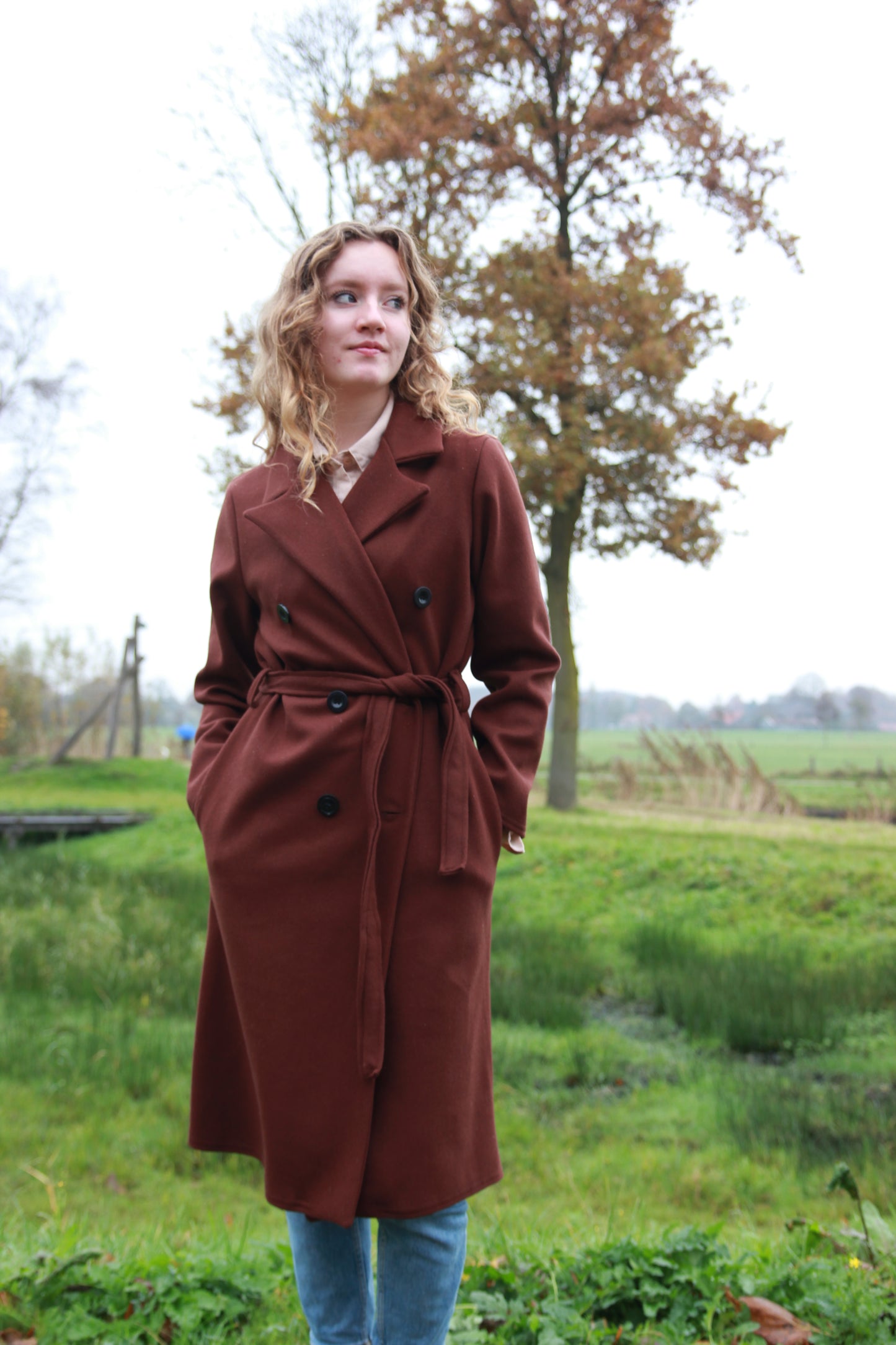 Trendy donkerbruine trenchcoat met brede kraag en scheve zakken aan de voorkant