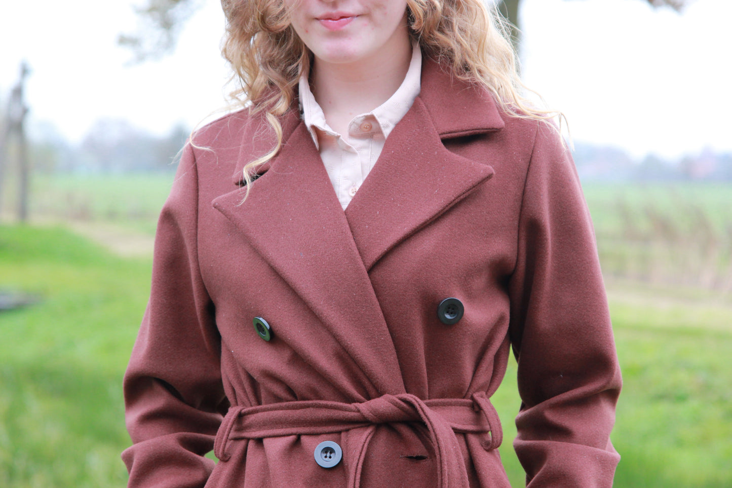 Close up van de knopen en tailleriem van de donkerbruine trenchcoat